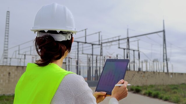 Engineer inspecting an electrical substation, using a digital tablet for data analysis and managing the power grid with advanced technology and smart energy solutions