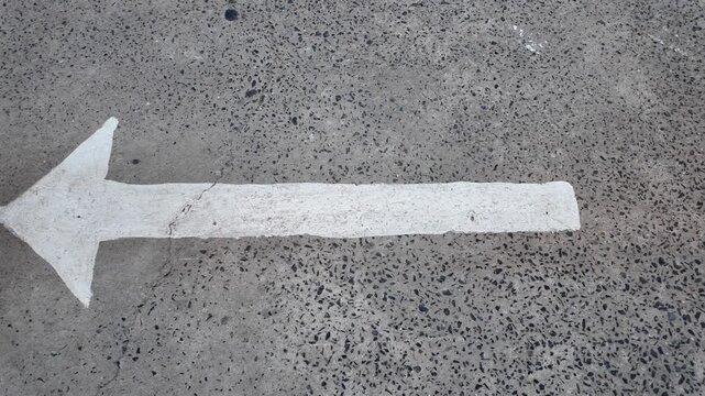 Large white arrow painted textured concrete pavement, indicating direction and providing guidance. This bold symbol stands out against rough surface, enhancing road navigation with its clear texture.