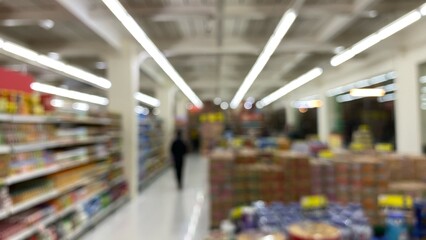 Fototapeta premium A blurry supermarket interior with bright lighting and aisles of products on the left and right. A modern setting with a bokeh effect.