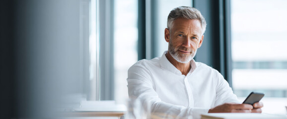 Fototapeta premium Mature businessman using smartphone indoors