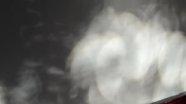 Slow motion handheld pan of light reflections shifting and drifting across interior wall near window in dim evening room