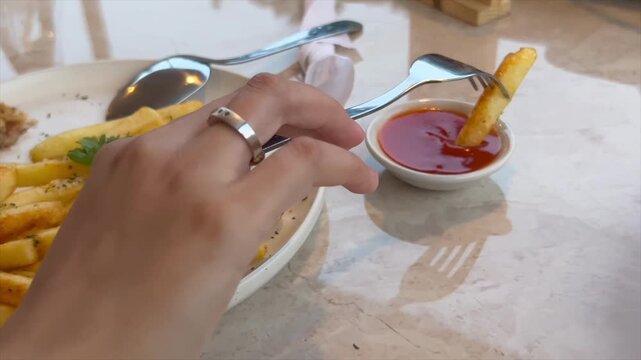 Close up of a person dipping crispy french fries into chili sauce with a fork