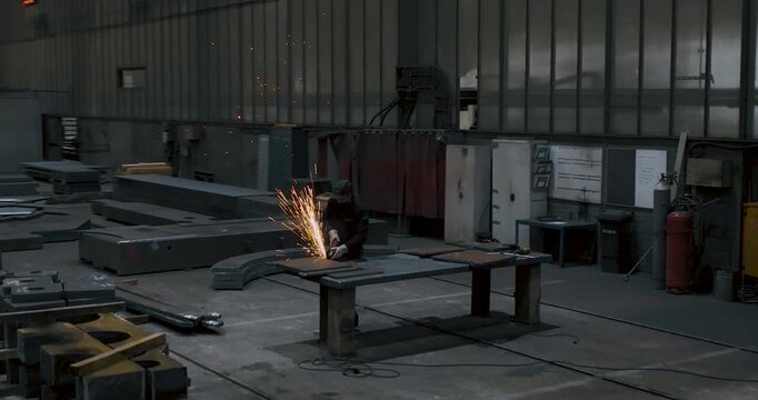 Wide view of a factory worker grinding metal parts with bright sparks in an industrial workshop