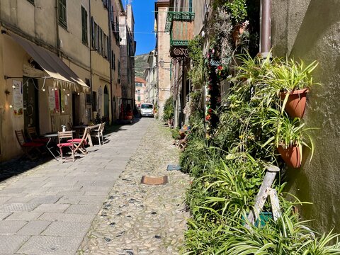 A charming street scene in Finalborgo, Italy, with colorful buildings and abundant potted plants, 30.03.2026.