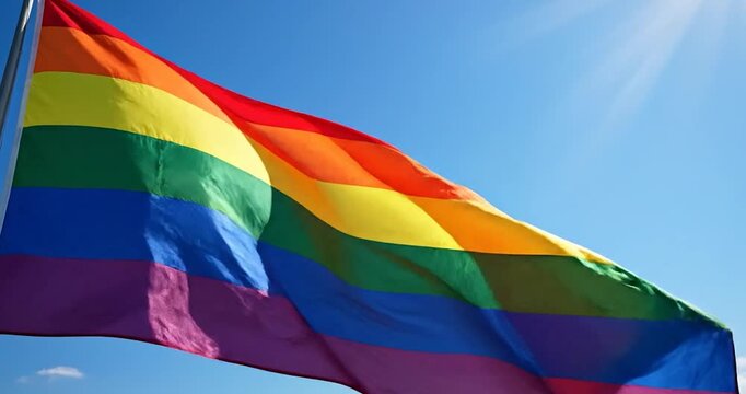 Rainbow pride flag waving against blue sky with bright sunlight flare