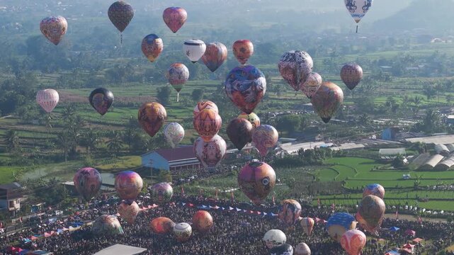 Epic Aerial Balloon Festival with Dozens of Colorful Balloons in Flight. A breathtaking aerial spectacle of dozens of hot air balloons soaring above a massive crowd during a vibrant festival.