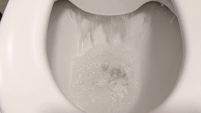 A top view of a toilet being flushed with water swirling rapidly in the bowl. The white porcelain toilet contrasts with the dynamic movement of the water