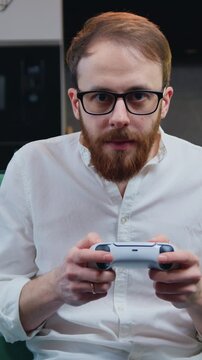 Middle age smilling man playing video game in moderm kitchen apartment enjoying indoor activity. Online entertainment and leisure activity concept.