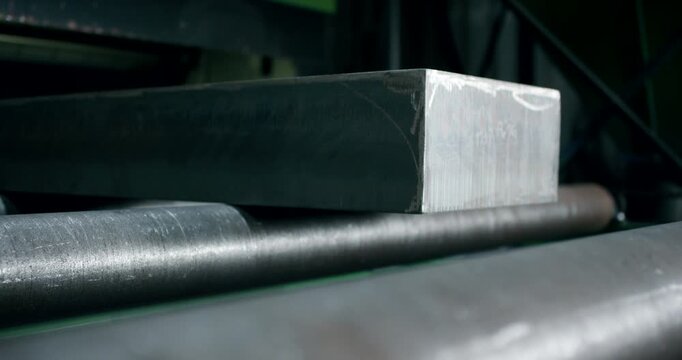 Close up of a solid steel billet moving on a metal roller conveyor in a heavy industry factory