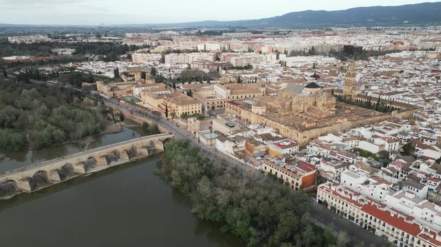 Drone pulls back to reveal the historic center of Cordoba with the Guadalquivir River on an overcast day, Andalusia, Spain.