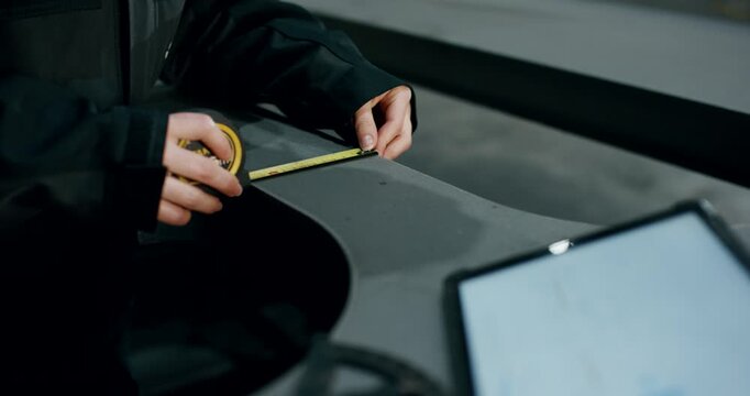 Close up of factory worker hands using a tape measure on a metal part with a tablet in the foreground