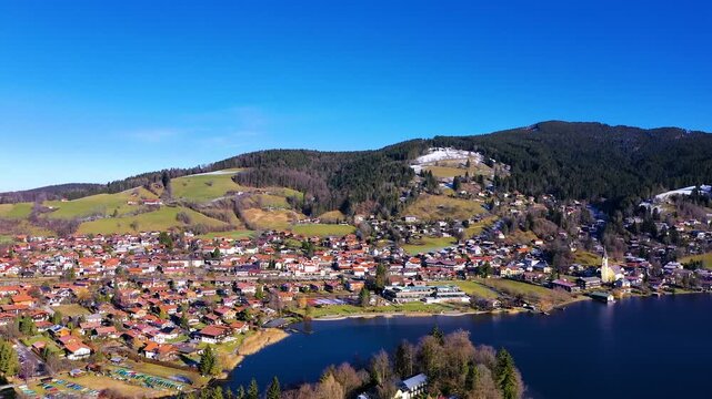 Drohne steigt &uuml;ber Schliersee mit Blick auf Dorf und Alpenlandschaft im sonnigen Winter in 4K