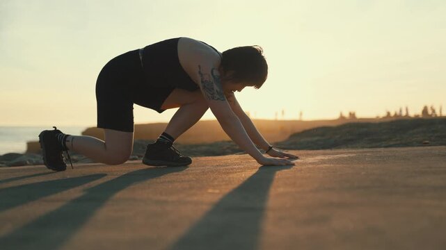 Athletic woman doing burpee exercise at sunset