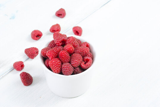raspberry fruits at white ceramic cup, on bright wood table