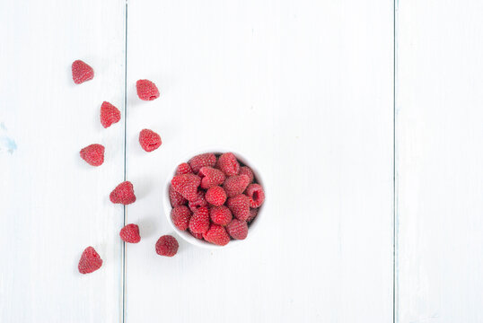 raspberry fruits at white ceramic cup, on bright wood table