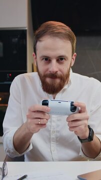 Middle age smilling man playing video game in moderm kitchen apartment enjoying indoor activity. Online entertainment and leisure activity concept.