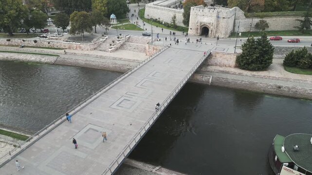 Drone descends to reveal a wide historic pedestrian bridge crossing the Nisava River in central Nis, Serbia.