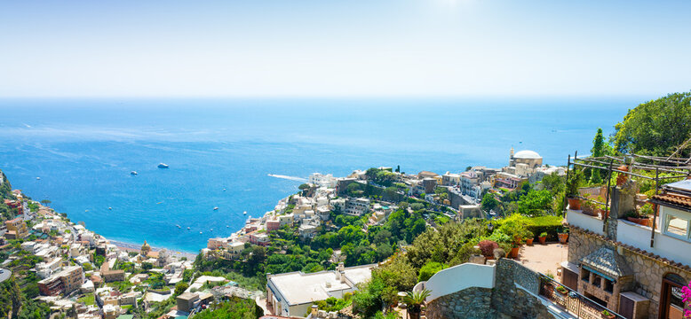 Panoramic view of Positano on Amalfi Coast, Italy with colorful buildings cascading down hillside toward turquoise Mediterranean waters. Lush vegetation frames traditional architecture of Positano 