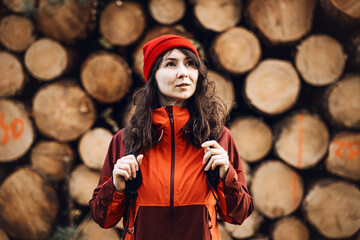 Obraz premium Woman with backpack stands in front of stacked logs while looking away. female hiker trekking, outdoor adventure lifestyle, solo traveler adventure.