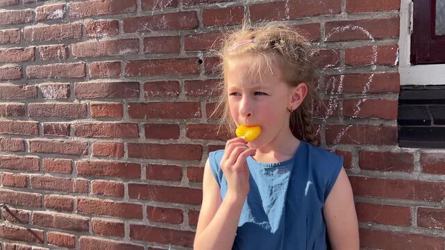 A young girl licks a popsicle on a sunny day, squinting her eyes and sticking out her tongue in a joyful summer moment. Children's advertising campaigns, summer snack promotions, parenting blog