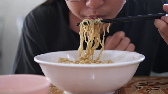 Close-up of young woman eating delicious instant noodles with chopsticks from a white bowl