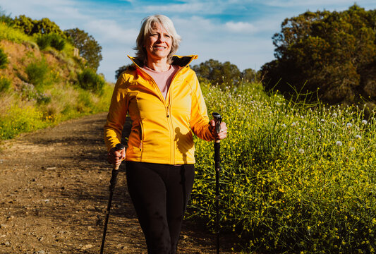 Active senior woman hiking on outdoor trail using trekking poles