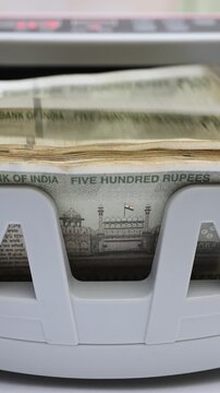 Macro shot of banknote counting machine with Indian rupee (INR) money. Automatic currency counter equipment processing 500 rupees with Red Fort vignette. Finance and banking industry in India.