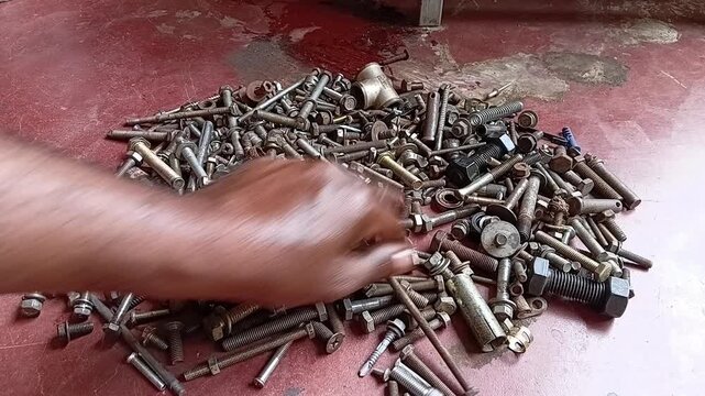Close-up of oily mechanic hands selecting and screwing a matching nut onto a bolt from a pile of old rusty hardware. Concept of perfect fit, compatibility, and finding a solution.