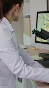 Vertical shot of bicultural young geneticists in white coats conducting medical research on microscope while analyzing molecules in smart lab
