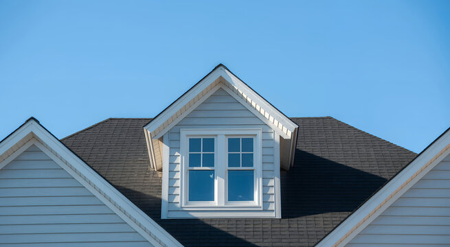 Exterior view of a residential house roof with a dormer window against a clear blue sky background