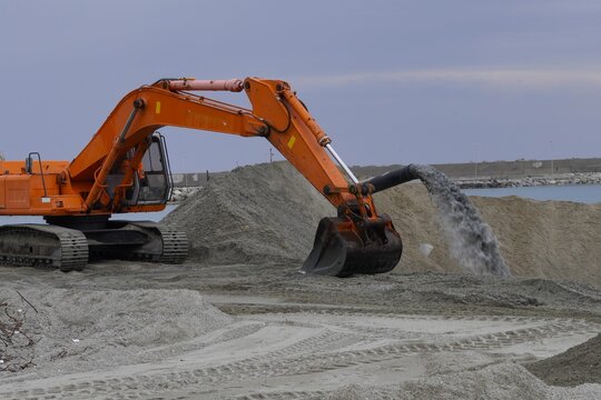 Industrial cleaning, sand washing. A large industrial pipe through which a mixture of water and sediment is discharged onto a sand embankment during construction or dredging operations on the coast.
