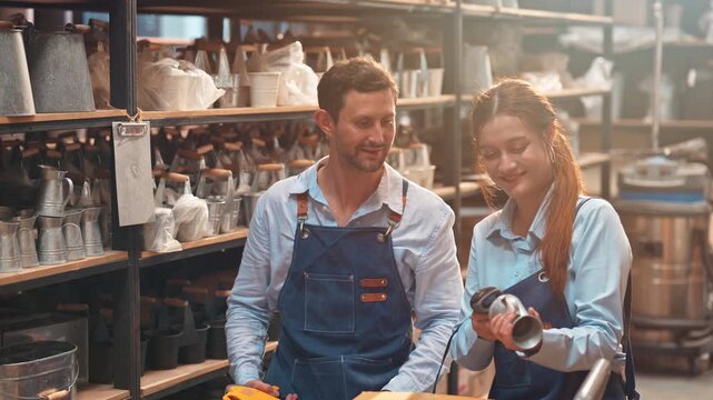 Man and woman in aprons work together to scan product barcodes for inventory management in a modern, organized workshop or storeroom.