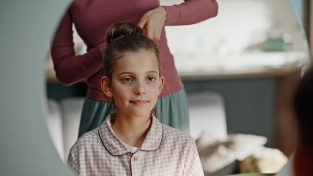 Home kid looking mirror having hairstyle routine closeup. Mother doing hair bun