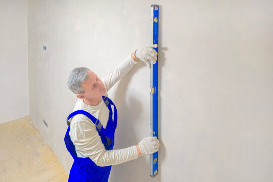 The builder checks the verticality of the plastered surface.