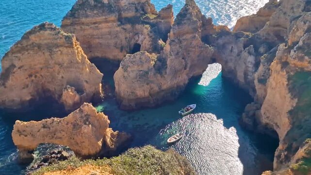 Portugal Algarve 4k video top view of Praia da Marinha yellow cliffs and boats sailing through rock arches. Scenic Atlantic ocean coast with turquoise water in Lagoa. Summer travel scenery