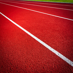 Fototapeta premium Close-up of a red running track with white lane lines. Strong texture and perspective create a dynamic athletics and sports background.
