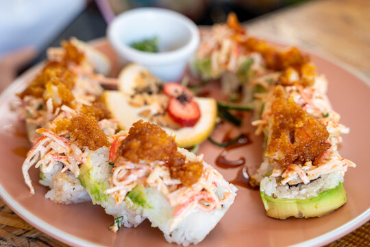 Close-up of sushi rolls topped with shredded crab, avocado, and crispy flakes, served on a plate with sauce and garnish in a restaurant setting