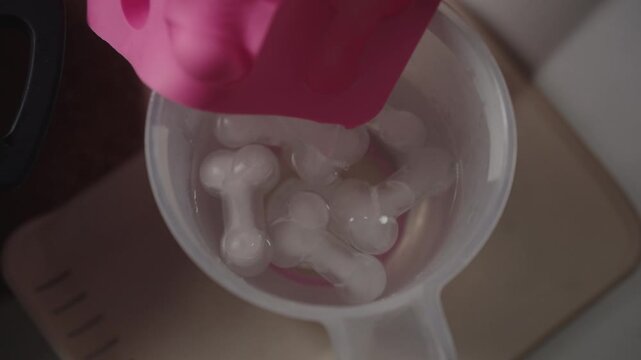 Hands removing phallic shaped ice cubes from silicone mold, fun and unique concept for parties, celebrations, and novelty drinks, adding humorous touch to any event.