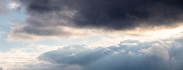 Obraz premium Panoramic stormy sky with contrast of dark and light clouds and sunbeams, dramatic atmosphere before thunderstorm