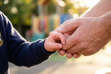 Fototapeta premium Child holding adult hand in sunlight at a playground 