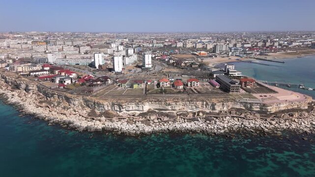 Scenic aerial footage of Aktau coastline showcasing luxury cottages on rocky cliffs and modern high-rise buildings. The shot features the iconic Rock Trail wooden boardwalk, a premier tourist 