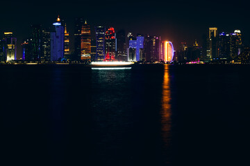 Fototapeta premium Stunning long exposure view of the illuminated skyline of Doha at night, featuring modern skyscrapers glowing with vibrant colors and reflections shimmering across the calm waters of the Arabian Gulf.