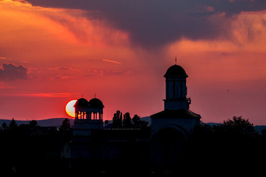 Sunset behind a church with a clock tower and a sun setting. Unfolds beneath the open sky across Sibiu, Romania, spills across the sky