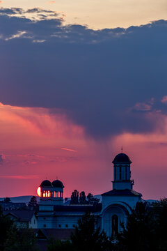 Sunset behind a church with a clock tower and a sun setting. Unfolds beneath the open sky across Sibiu, Romania, spills across the sky