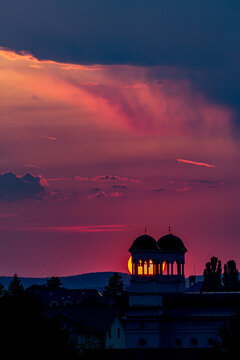 Sunset behind a church with a clock tower and a sun setting. Unfolds beneath the open sky across Sibiu, Romania, spills across the sky