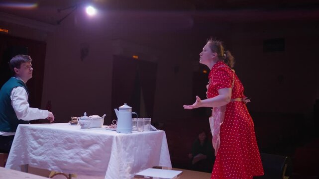 Amateur stage performance with two actors in retro costumes at a small theater, conversing over a simple table setting under soft dramatic lighting