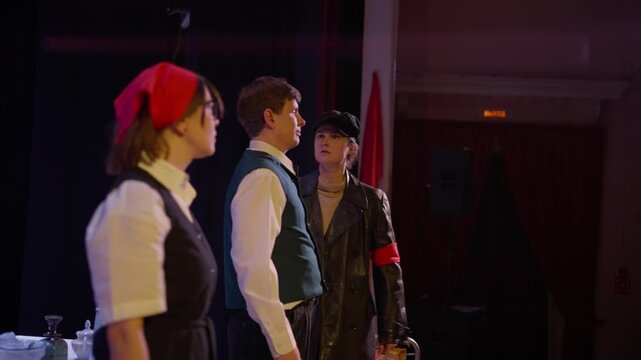 Amateur stage drama with three performers in vintage costumes acting an intense confrontation around a small table under theatrical lighting in a dim hall