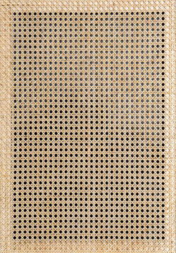 Rattan is pulled tight across a wooden frame, serving as a facade for furniture. The setup is found indoors, showcasing a minimalist design with natural materials