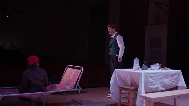 Amateur theater performance with actors in vintage costumes on stage, portraying an intense domestic drama around a table during a small community play