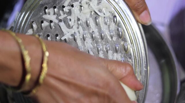 High angle shot of fresh white potato shreds being processed through a metal grater for traditional snack preparation.